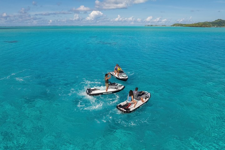 Three people on jet skis in clear blue ocean on a sunny day with distant shoreline.