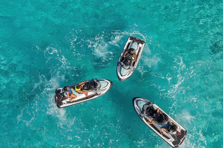 Three people on jet skis in blue water viewed from above.