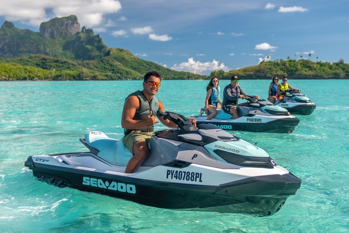 Four people riding jet skis on turquoise water with green hills in the background.