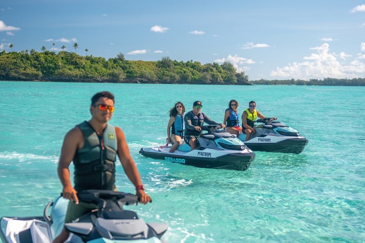 Four people on jet skis in turquoise water near a green island under a blue sky.
