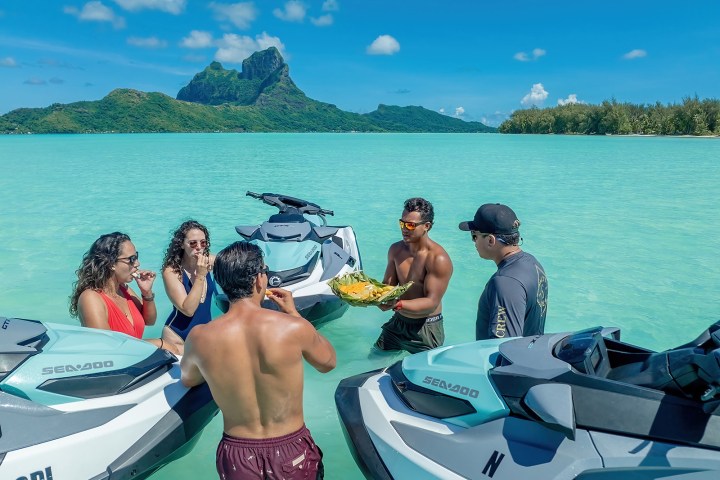Group of people on jet skis in turquoise water with mountain view.