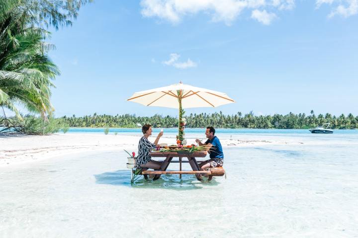 A couple having a lunch feet in the water on a motu in Bora Bora