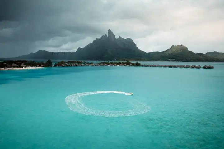 an island in the middle of a body of water with Bora Bora in the background